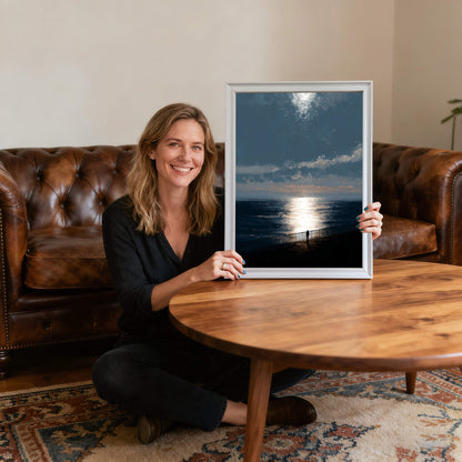 Smiling woman sitting on the floor holding the ocean sunset art print in a thin white wood frame, providing scale and showing the artwork's size relative to a person in a living room."
1 (10).jpg,