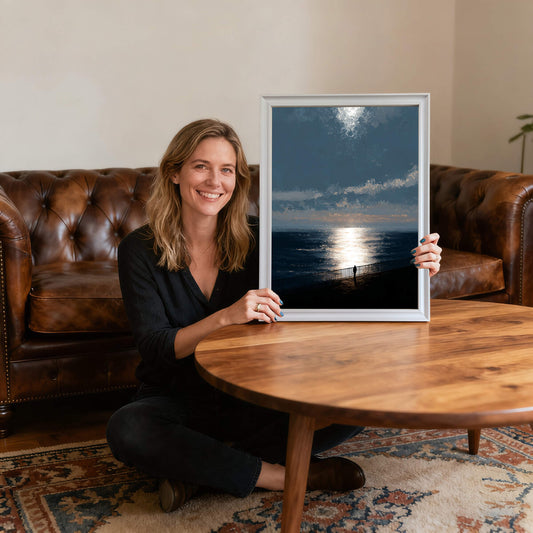 Smiling woman sitting on the floor holding the ocean sunset art print in a thin white wood frame, providing scale and showing the artwork's size relative to a person in a living room."
1 (10).jpg,