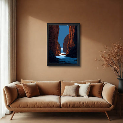 A framed art print of a striking red canyon and waterfall, hanging above a tan velvet sofa in a room with warm, earthy brown walls. The frame is black.