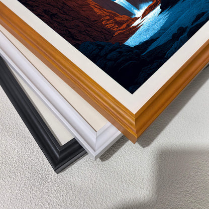 A stack of wood picture frame corners showing different color options: natural wood, white, cream/off-white, and black. A corner of the red rock canyon art print is visible on top.