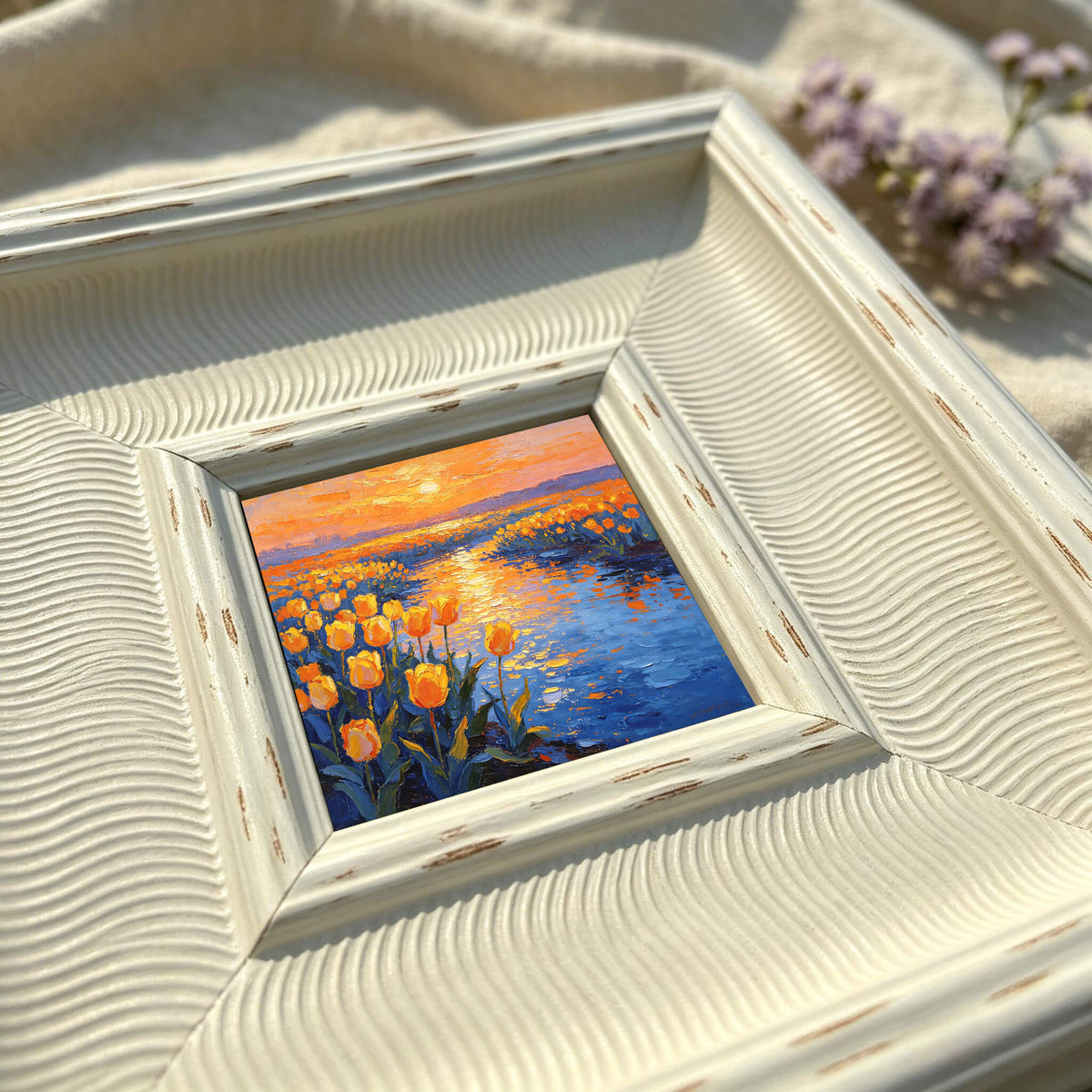  Square, off-white framed painting with a landscape scene. The artwork depicts a field of yellow tulips along a blue body of water, under an orange and yellow sunset. The frame has a textured, wavy design.