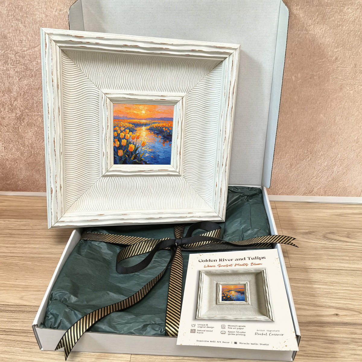 A framed oil painting of a landscape with a river and yellow flowers, presented in a white, textured frame. The painting is inside a gift box with a black and gold ribbon. The text on the card reads "Golden River and Tulips Where Sunlight Pretty Bloom."