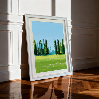 A framed art print of a green landscape with Cypress trees leaning against a white wainscoted wall on a glossy hardwood floor, brightly lit by sunlight. The frame is white.