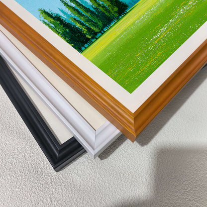 A stack of wood picture frame corners showing different color options: natural wood, cream/off-white, white, and black. A corner of the green meadow art print is visible on top.