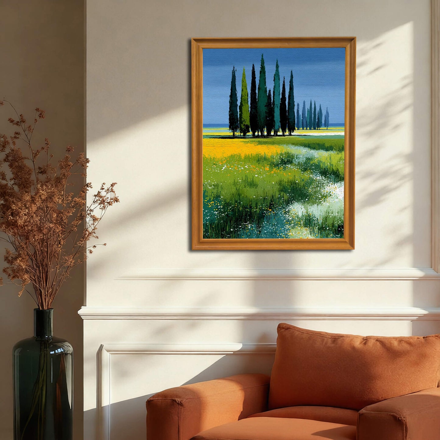 Art print of the cypress trees and field in a light wood (natural) frame, hanging on a light beige wainscoted wall above an orange armchair.