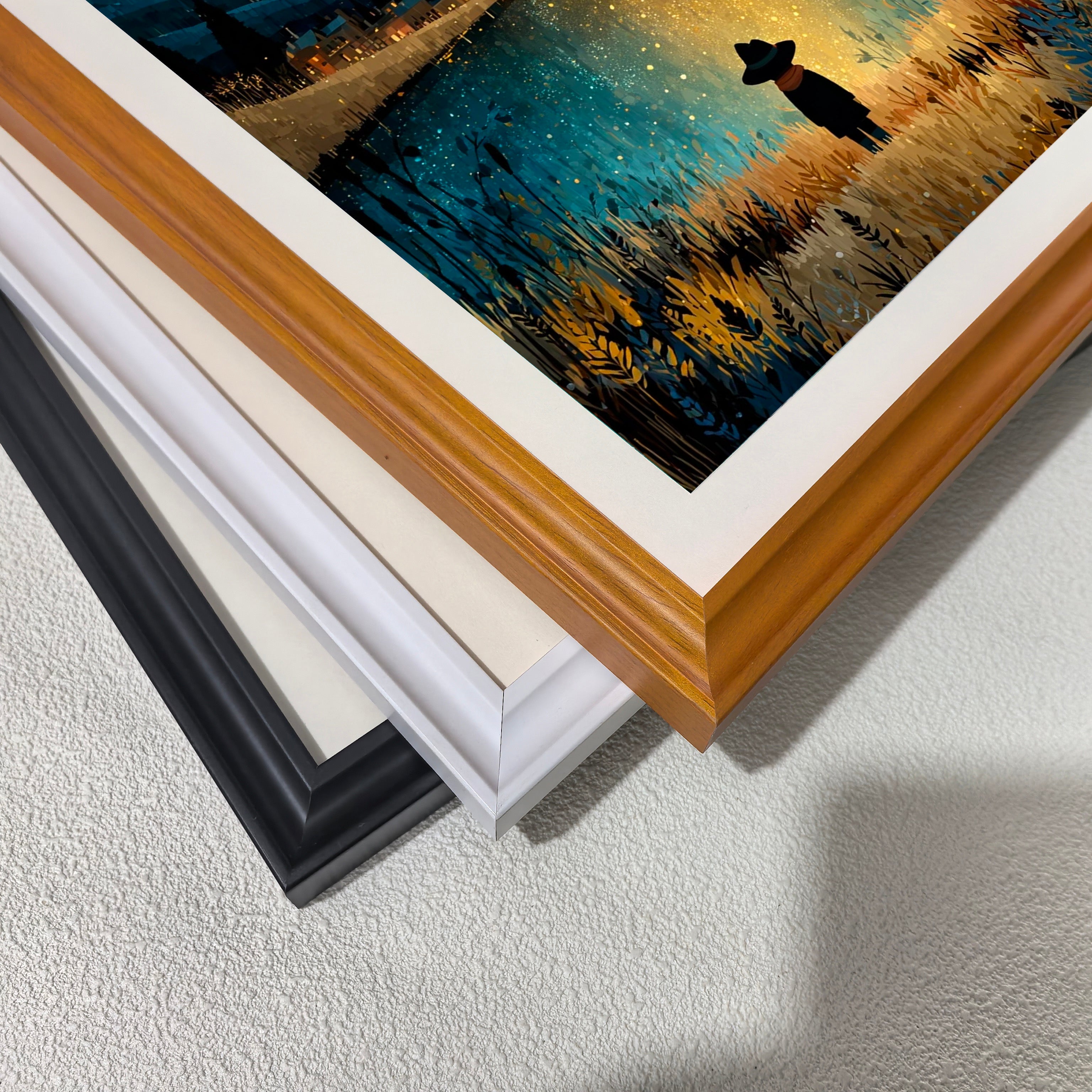 A stack of frame corners: black, off-white, white, and a light wood grain (brown). This displays the different framing options available for the moonlit lake art print.