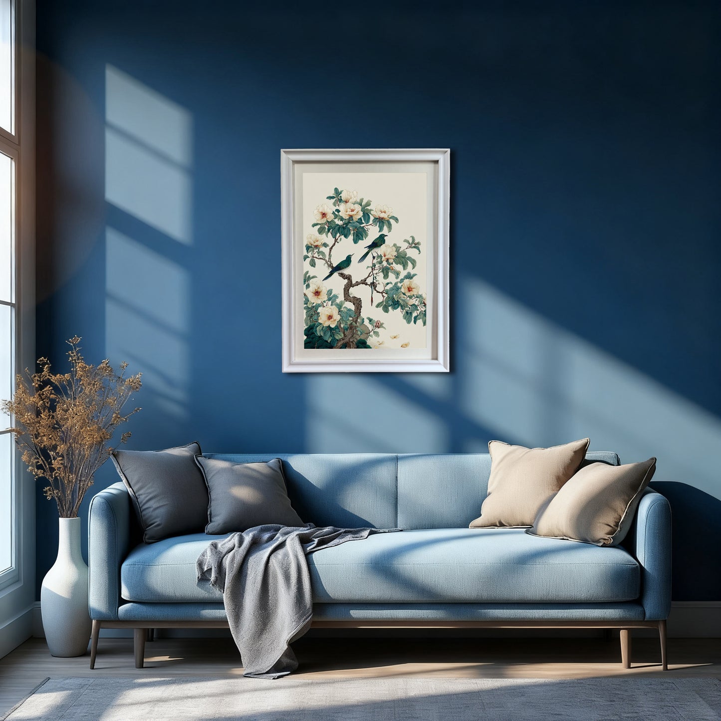 A wide interior shot of a minimalist living room with a navy blue wall; a white framed floral and bird print is centered above a light blue sofa with grey and tan pillows.