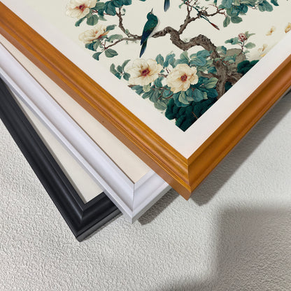 A close-up, angled shot showing the corners of three different picture frames—black, white, and light wood—stacked on top of each other over a textured white surface.