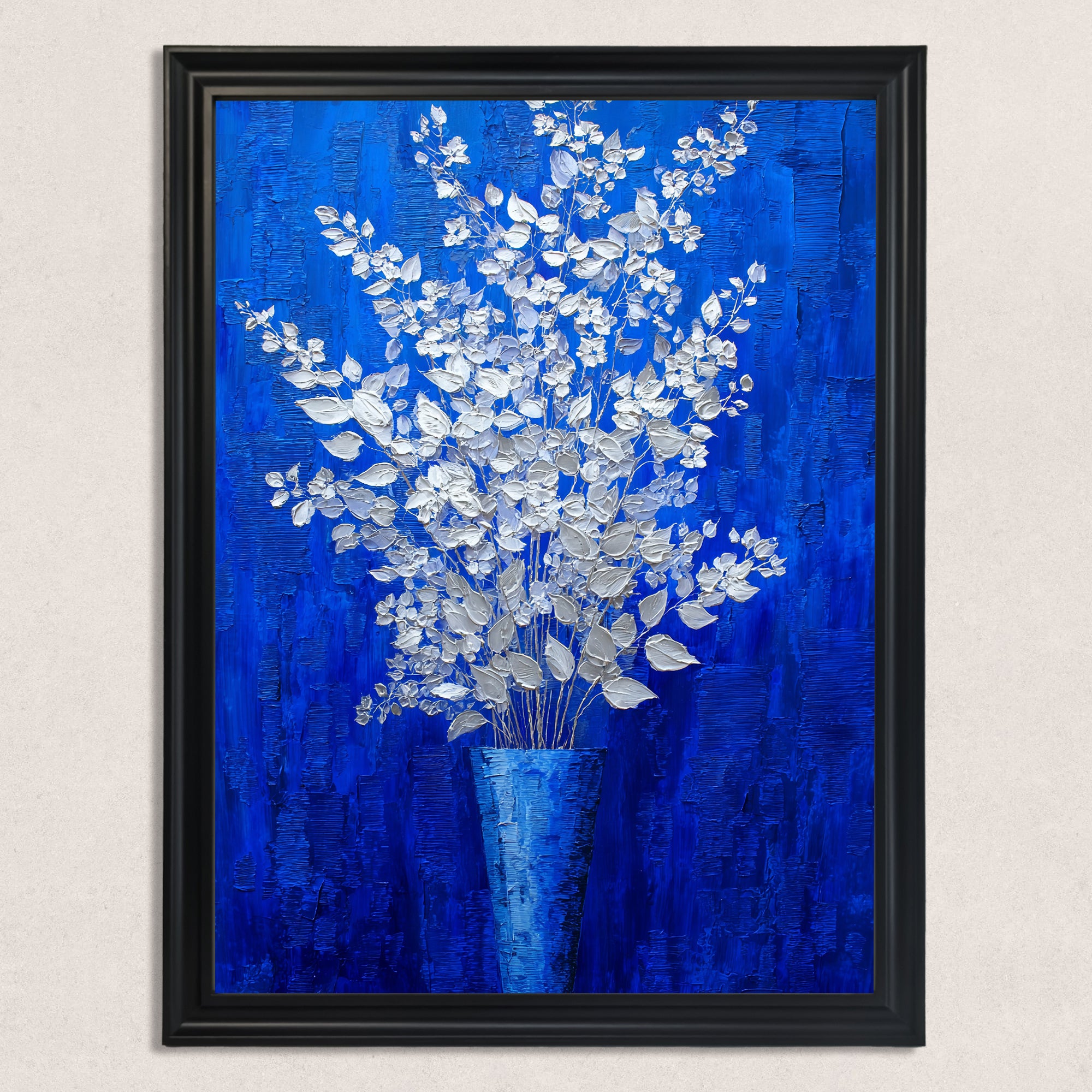 A vertical, rectangular oil painting of a silver-white floral arrangement in a blue vase, set against a rich, textured royal blue background, mounted in a black frame against a textured white wall.