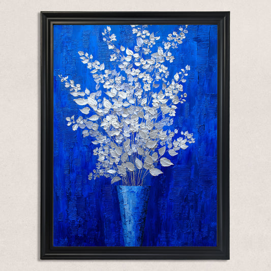 A vertical, rectangular oil painting of a silver-white floral arrangement in a blue vase, set against a rich, textured royal blue background, mounted in a black frame against a textured white wall.