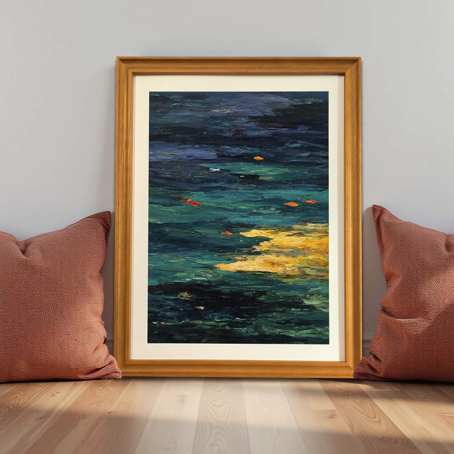 Abstract Goldfish Pond art print in a natural light wood frame (oak/maple), leaning against a gray wall on the floor between two terracotta-colored pillows, demonstrating a grounded decor style.