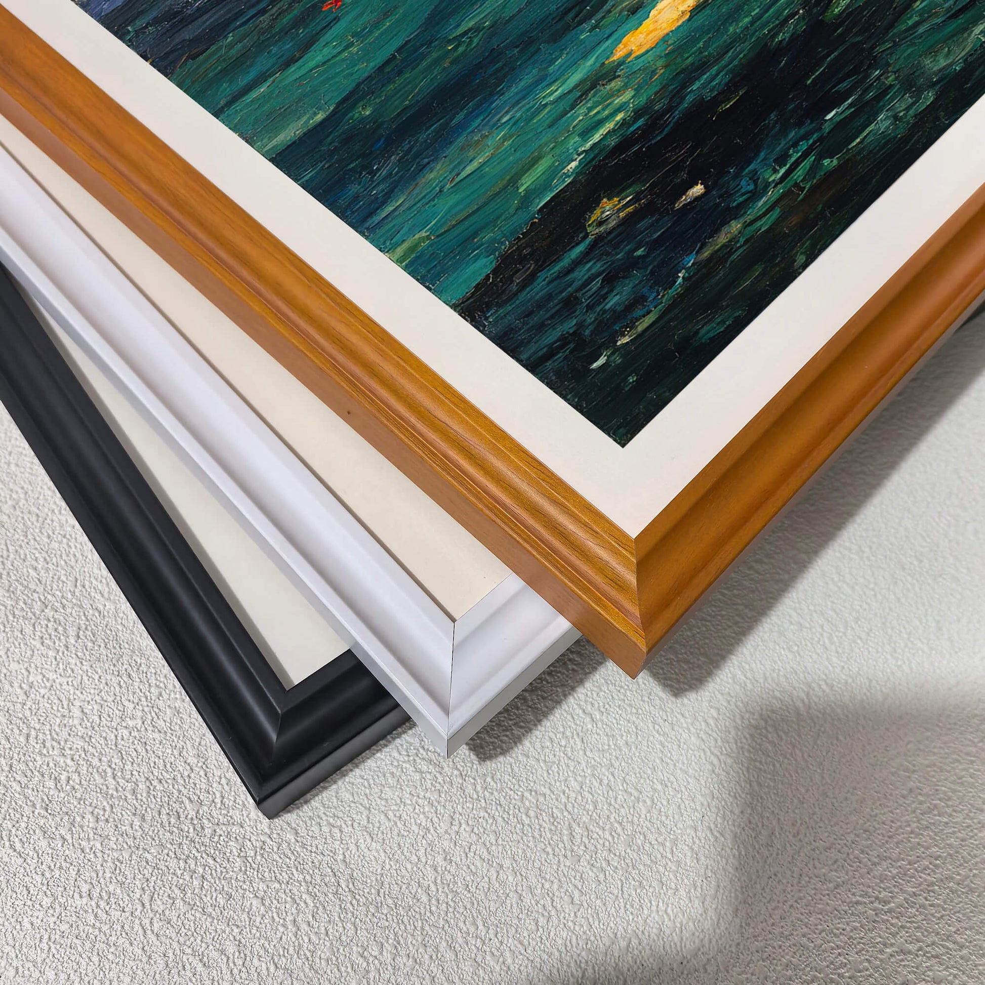 Stacked close-up of different wood frame options for art prints: black, white, and natural light wood (oak/maple). Shows the frame molding detail and finish against the dark art border.