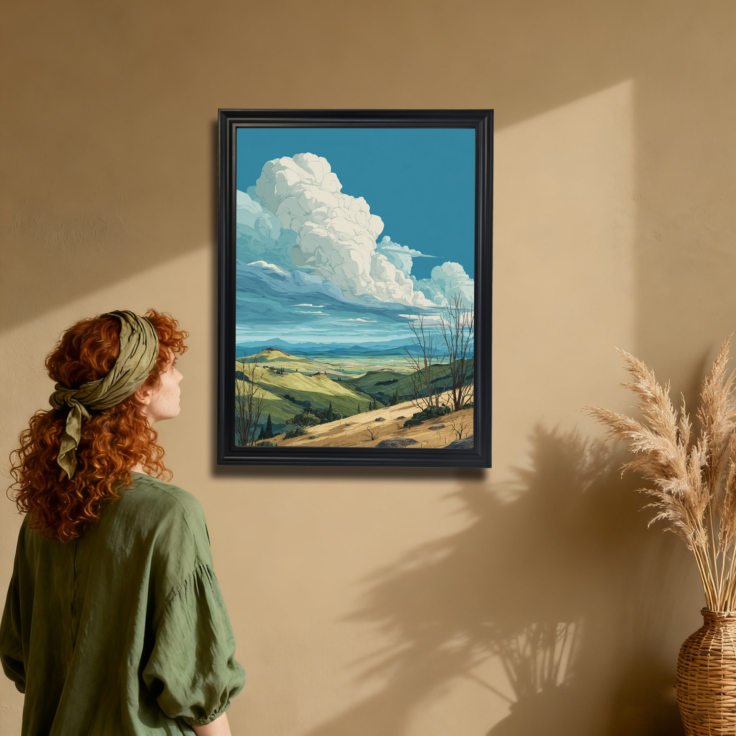 Rolling hills landscape art print in a black wood frame hanging on a tan wall. A woman in a green shirt is admiring the framed art, showing a boho or earthy interior decor style.