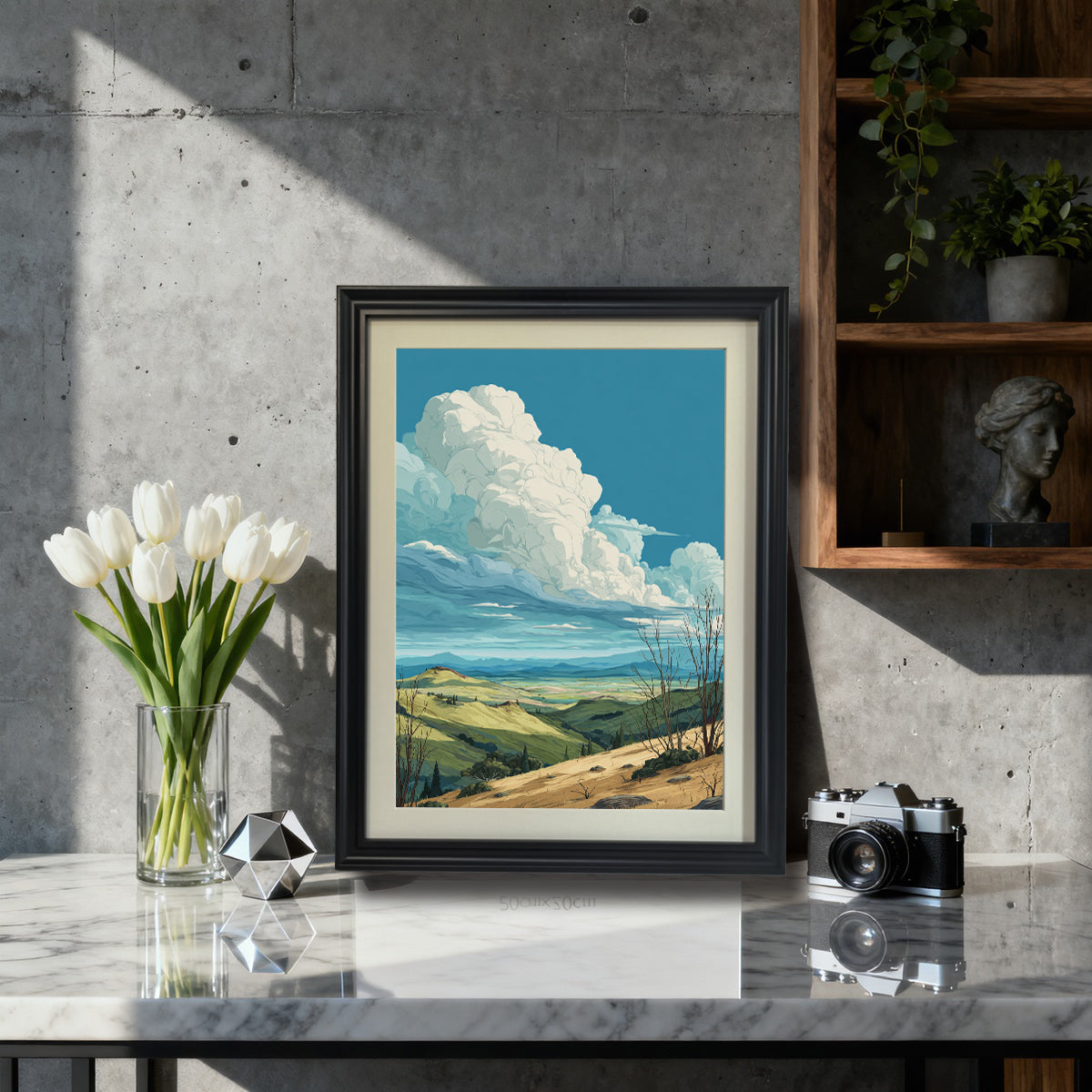Rolling hills landscape art print in a black wood frame with a mat, sitting on a marble countertop next to white tulips and a vintage camera, styled for modern or industrial decor.