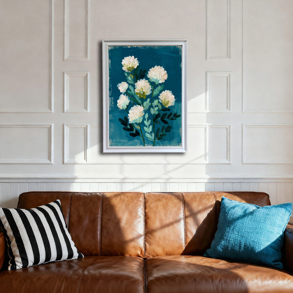 A white-framed art print hanging above a brown leather sofa. The white paneled wall provides a contrast to the deep teal-blue of the abstract floral artwork, which features white impasto flowers.