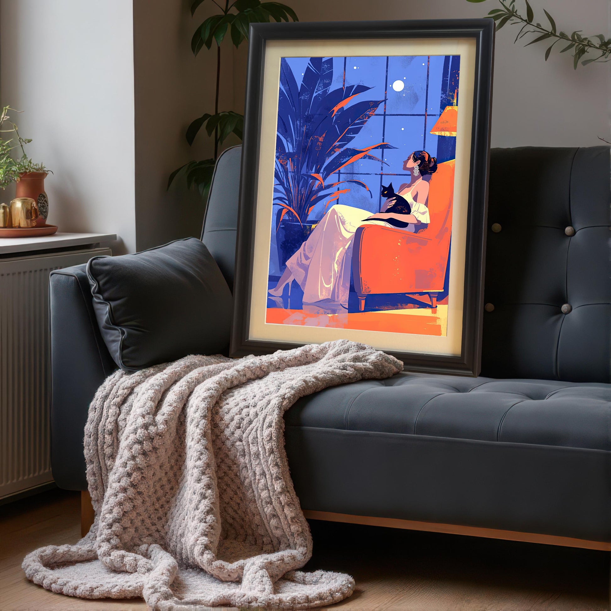 A framed art print of a woman and a cat propped up on a gray sofa with a knitted throw blanket.