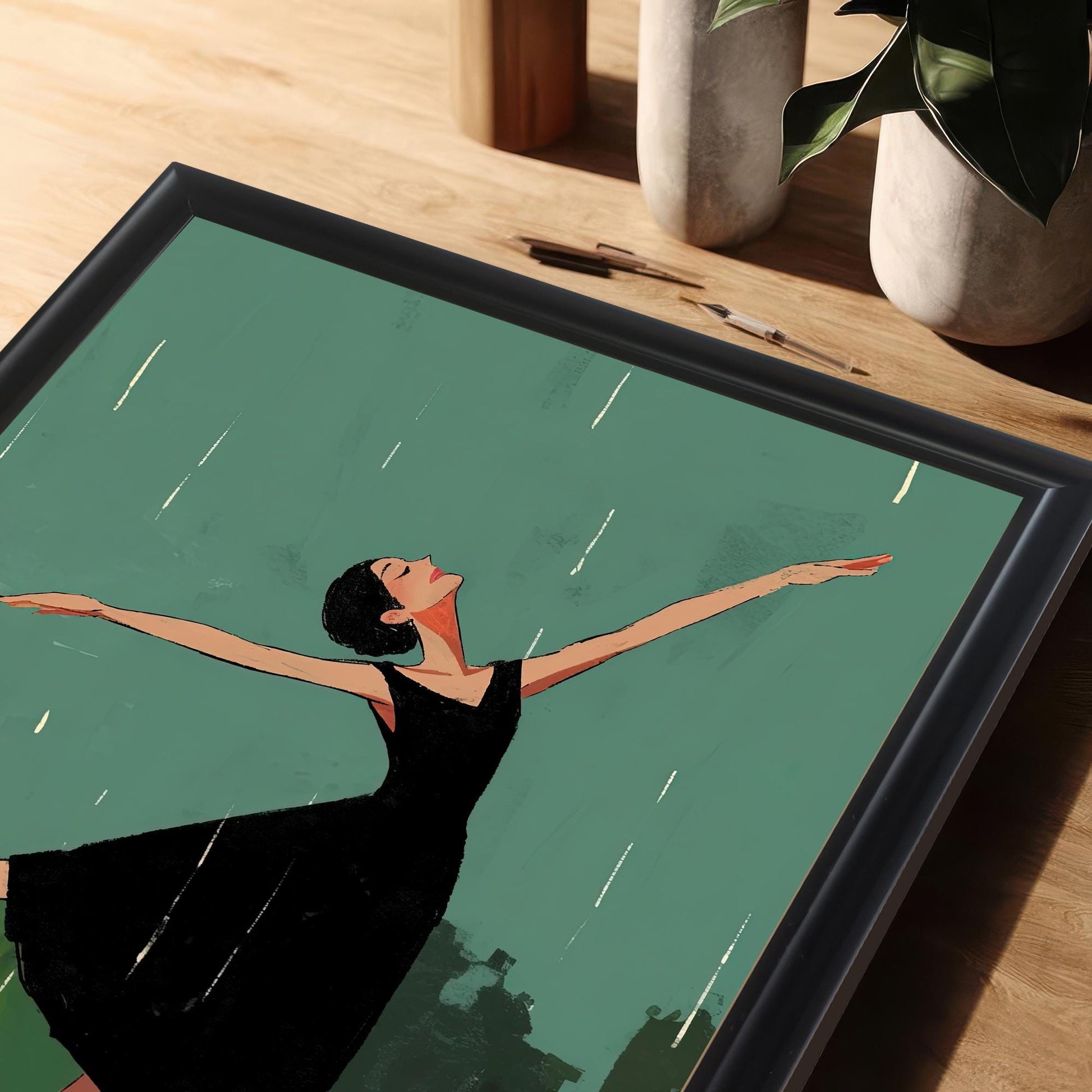 A close-up, angled shot of the framed art print, with the black frame and a portion of the dancing woman visible on a wooden table.