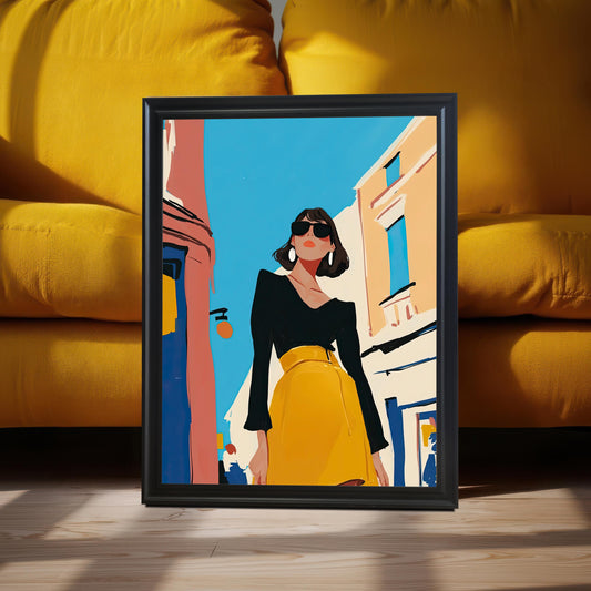 A framed art print with a black frame and no mat rests on a wooden floor, leaning against a mustard yellow sofa. The art depicts a stylish woman in a black shirt and yellow skirt standing on a street.