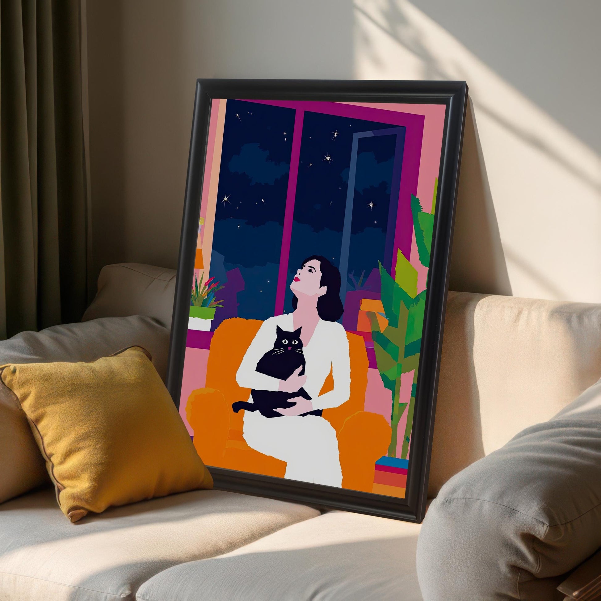 A large framed wall art print with a black wood frame, leaning against a wall on a light-colored couch. The print features a contemporary illustration of a woman and a cat gazing at the stars, adding a chic and artistic touch to a living room.