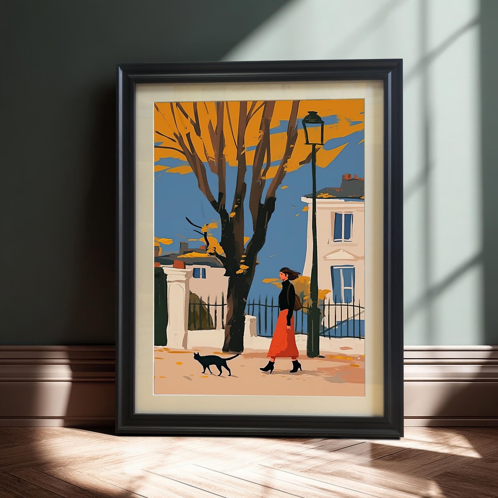 A framed art print of a person in a red skirt walking with a black cat on an autumn street, propped against a dark wall.