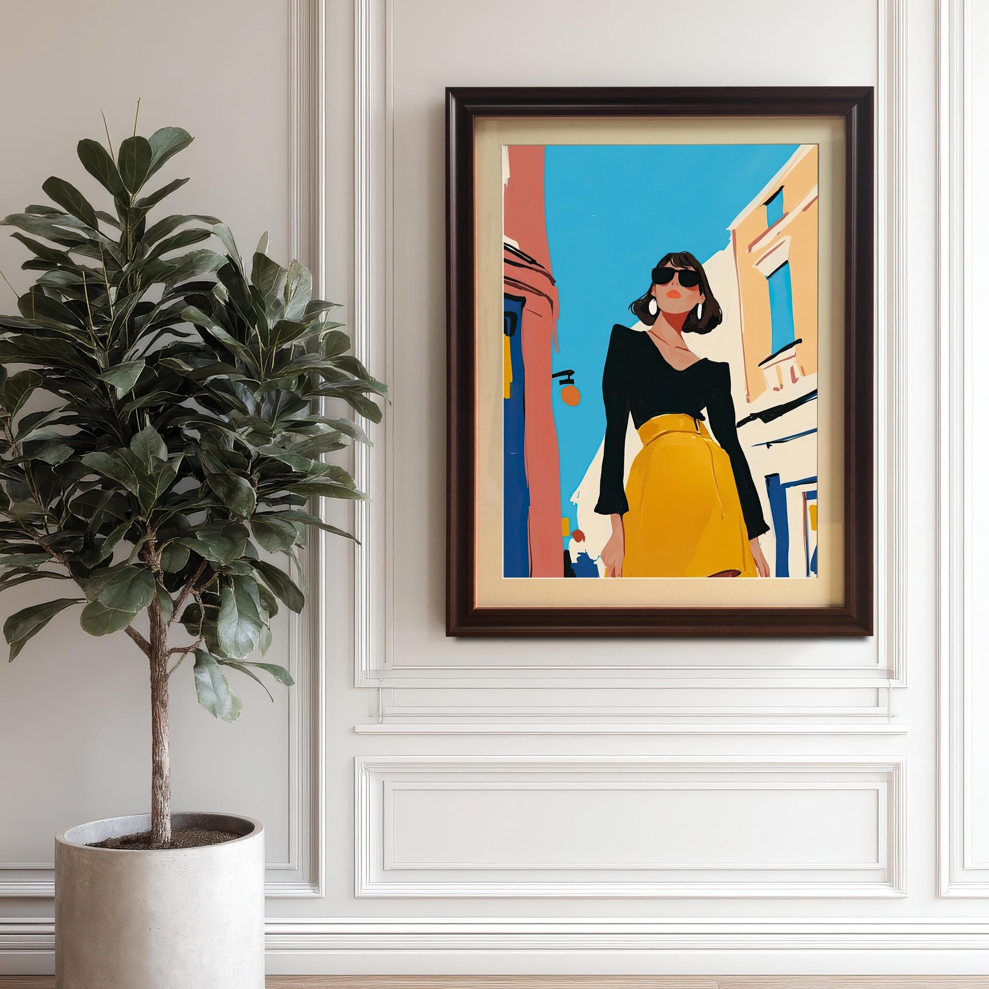 A framed piece of wall art hangs on a white paneled wall. The art depicts a stylish woman in a black shirt and yellow skirt standing on a street. The frame is a dark coffee brown. A large potted plant sits on the floor to the left of the frame.