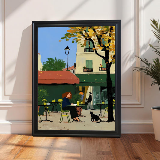 A framed artwork in a black frame leans against a wall on a wooden floor. The artwork depicts a woman sitting at an outdoor cafe table with a black cat nearby. The background features a building with a red awning and a tree with yellow autumn leaves. A potted plant is on the right.