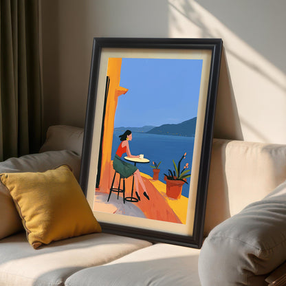 Framed wall art print propped on a beige sofa with a yellow pillow. The artwork shows a woman on a balcony with a beautiful ocean view, framed in a dark brown wood frame with a mount.