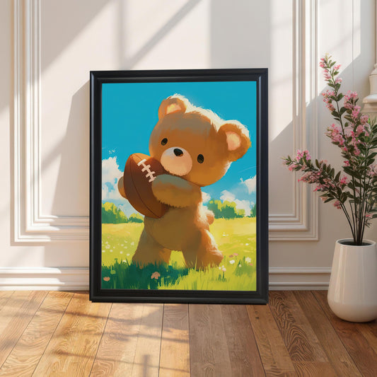 A framed wall art print of a teddy bear with a football, set in a black frame, stands on a wooden floor against a white paneled wall. Sunlight casts a shadow, and a plant with pink flowers is on the right.