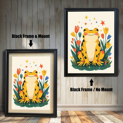 Two versions of a happy yellow frog wall art print with a black wood frame. The print on the left is a smaller size framed with a white mount (or mat), and the one on the right is a larger size without a mount. The image shows the framed print hanging against a white paneled wall.