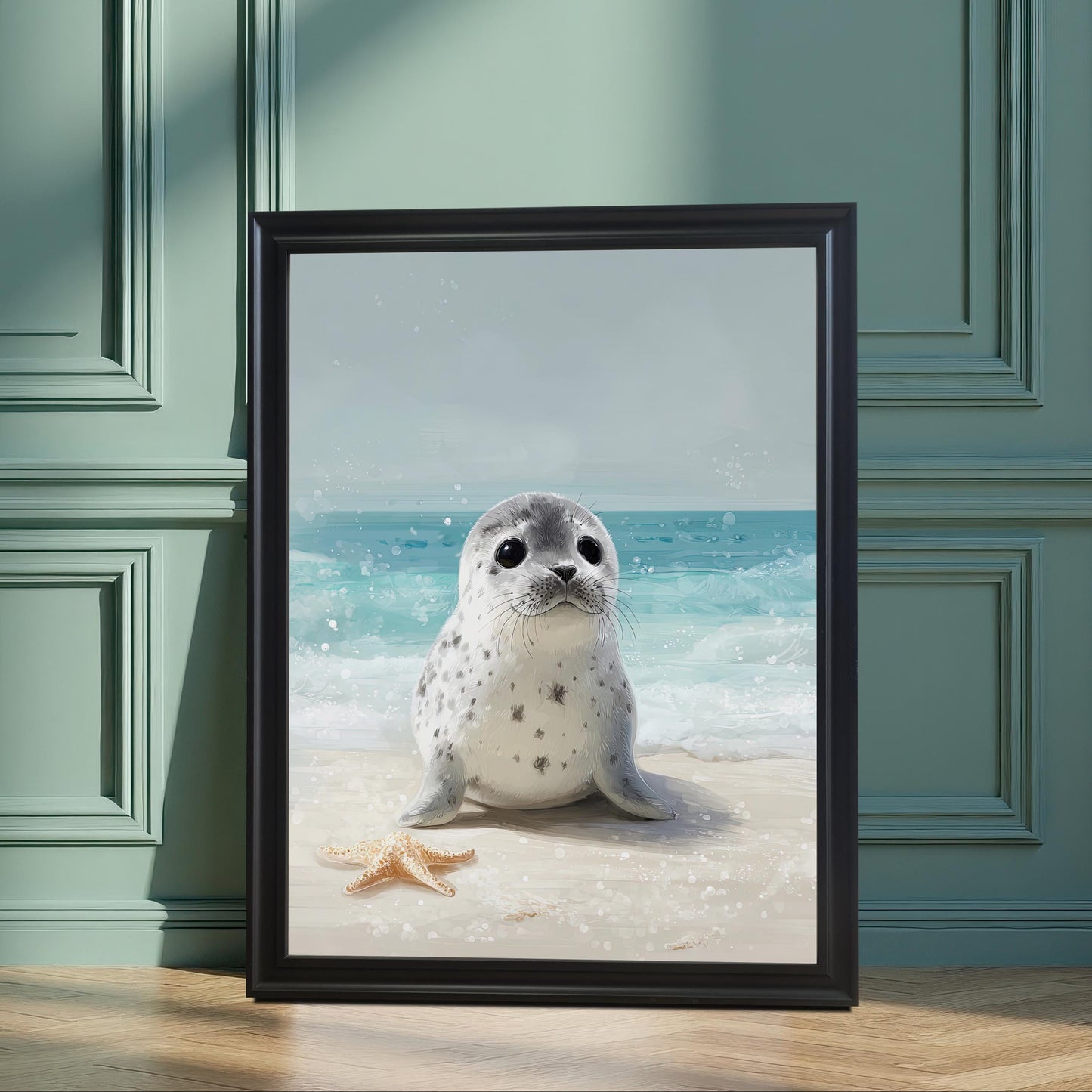 A framed art print of a cute baby seal on a beach, in a black frame. The print is propped on a wooden floor against a paneled teal-green wall, creating a serene, stylish feel.