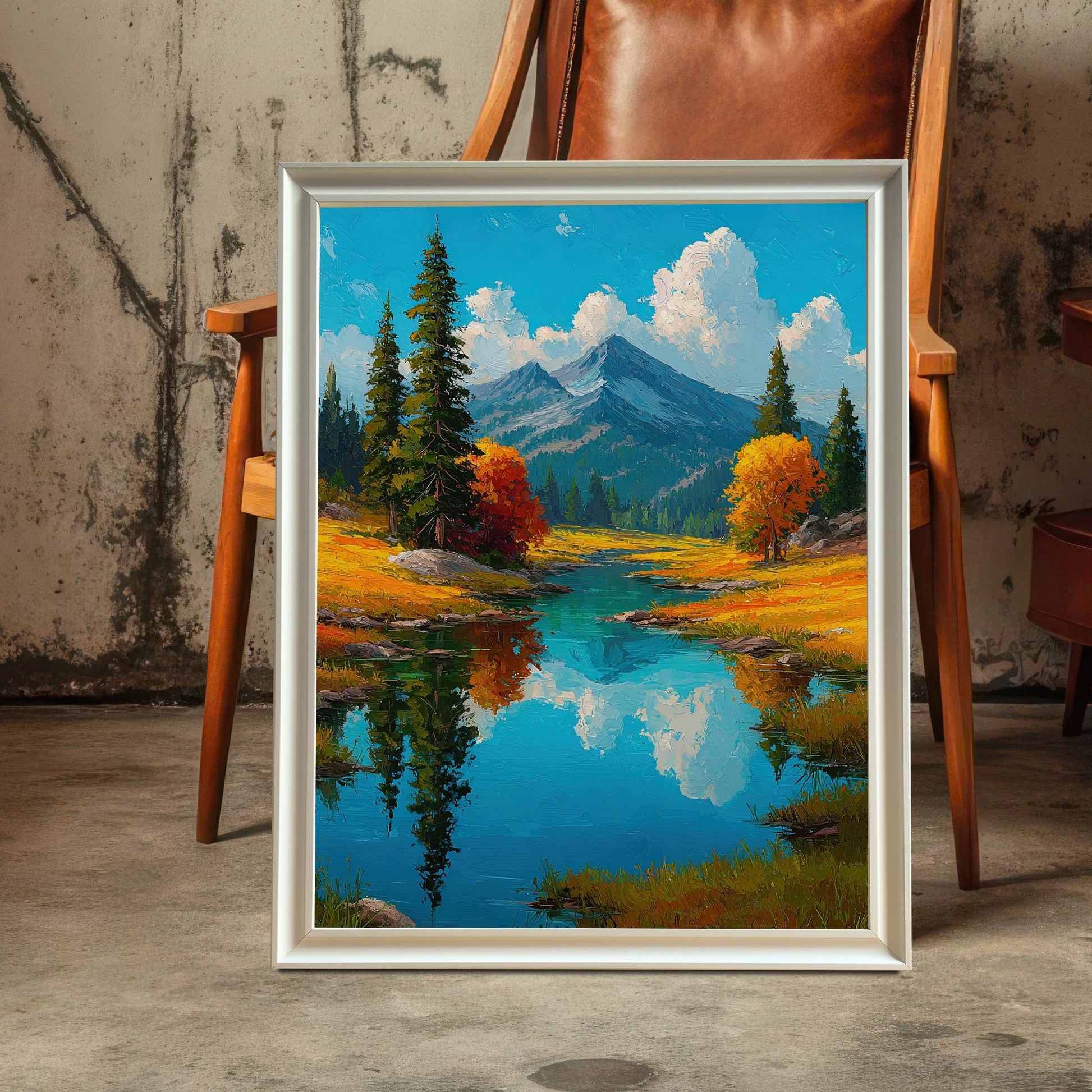 A framed art print with a white frame leans against a brown leather chair. The print shows a tranquil landscape with a lake, mountains, and trees.