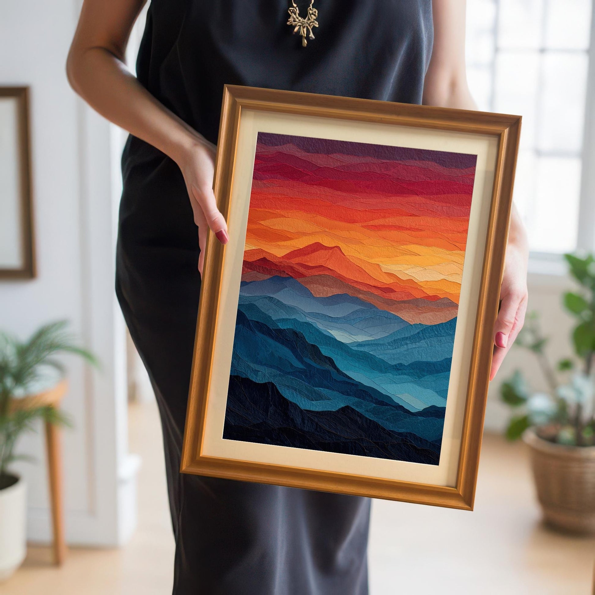 A person wearing a black dress holds up a framed painting of a mountain landscape with a golden frame and a mat board. The painting features blue mountains and a red and orange sky.