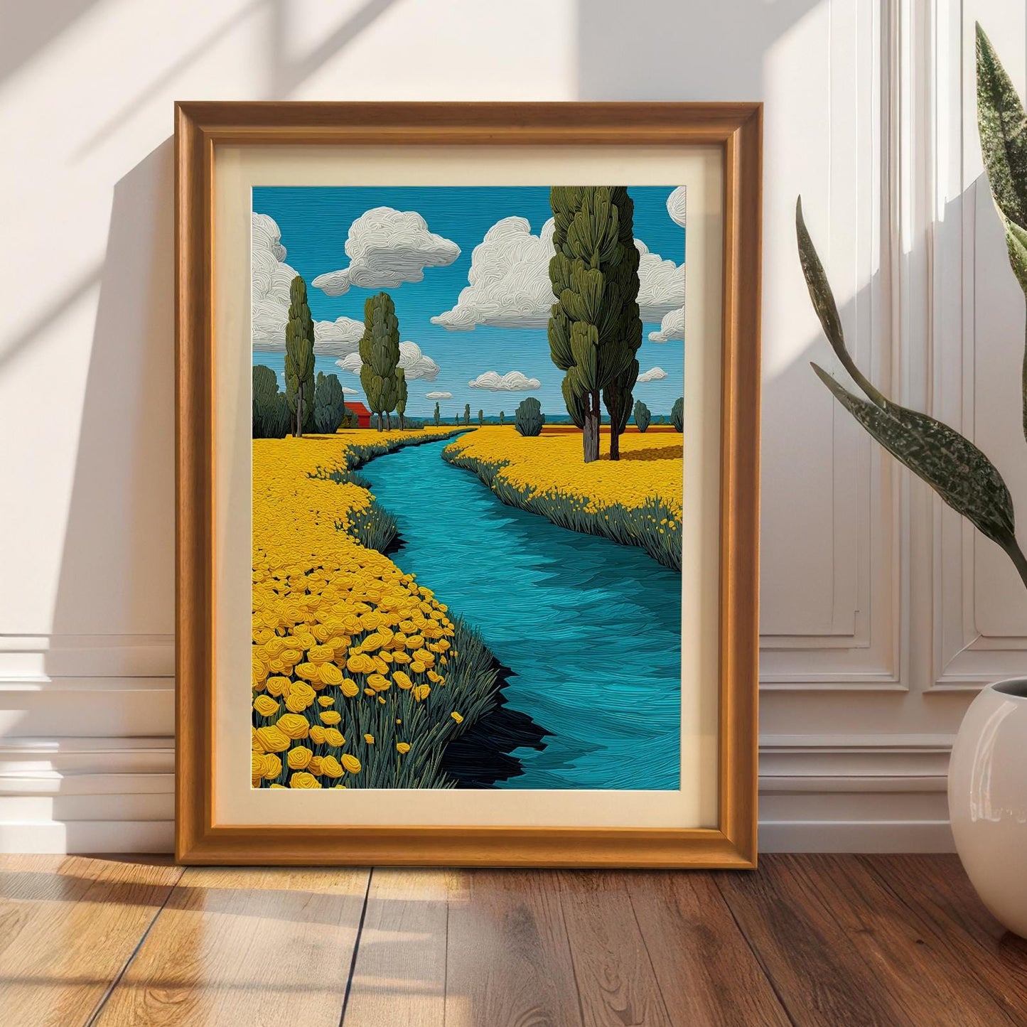 A framed painting of a river flowing through a field of yellow flowers. The painting, in an orange frame with a mount, is leaning against a white wall next to a large potted plant.