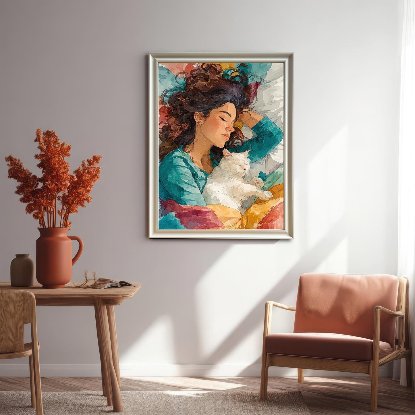 An art print of a woman with her eyes closed, holding a white cat. The artwork is framed in white and hangs on a light-colored wall above a wooden chair.