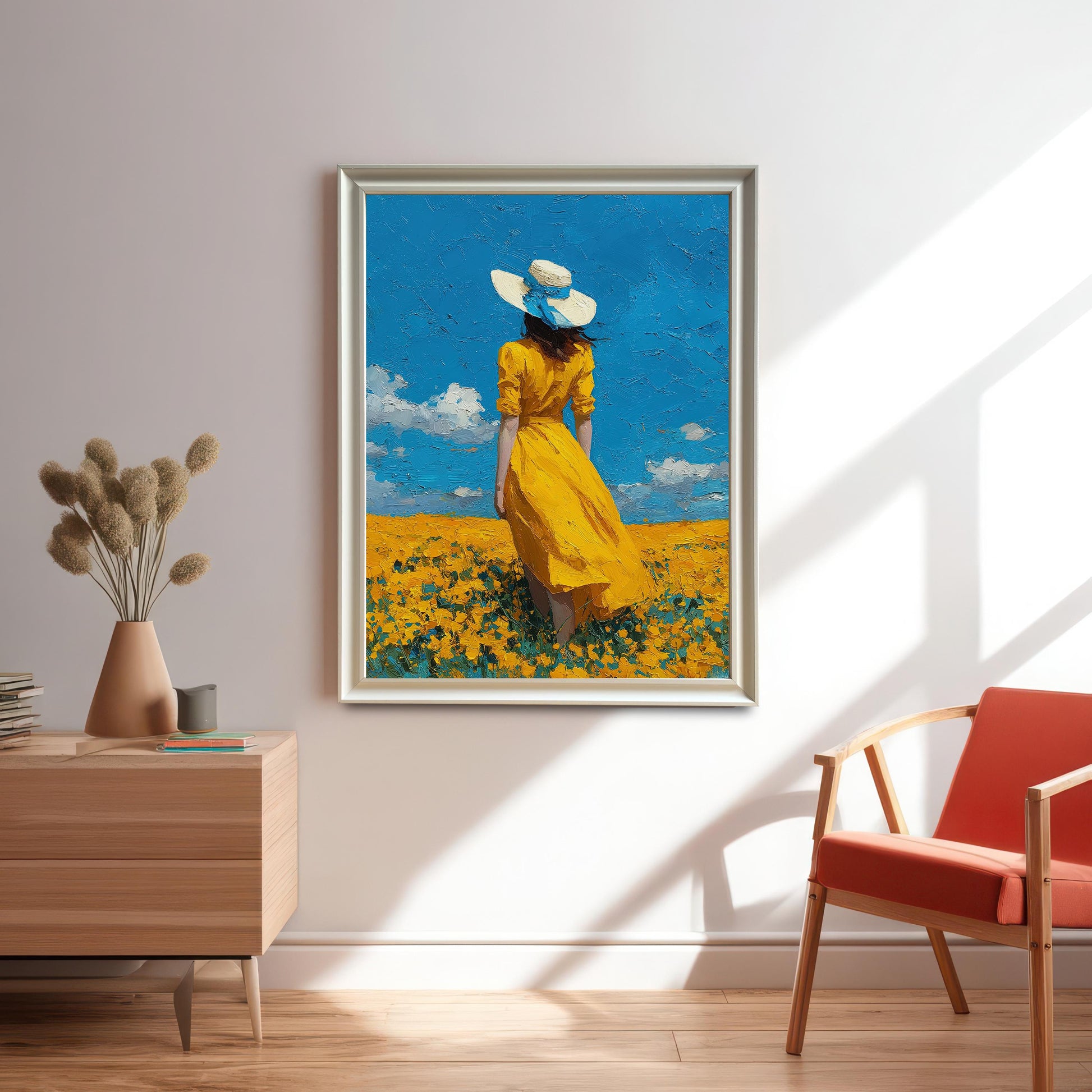 A white-framed art print of a woman in a yellow dress standing in a flower field, hanging on a white wall above a wooden console table.