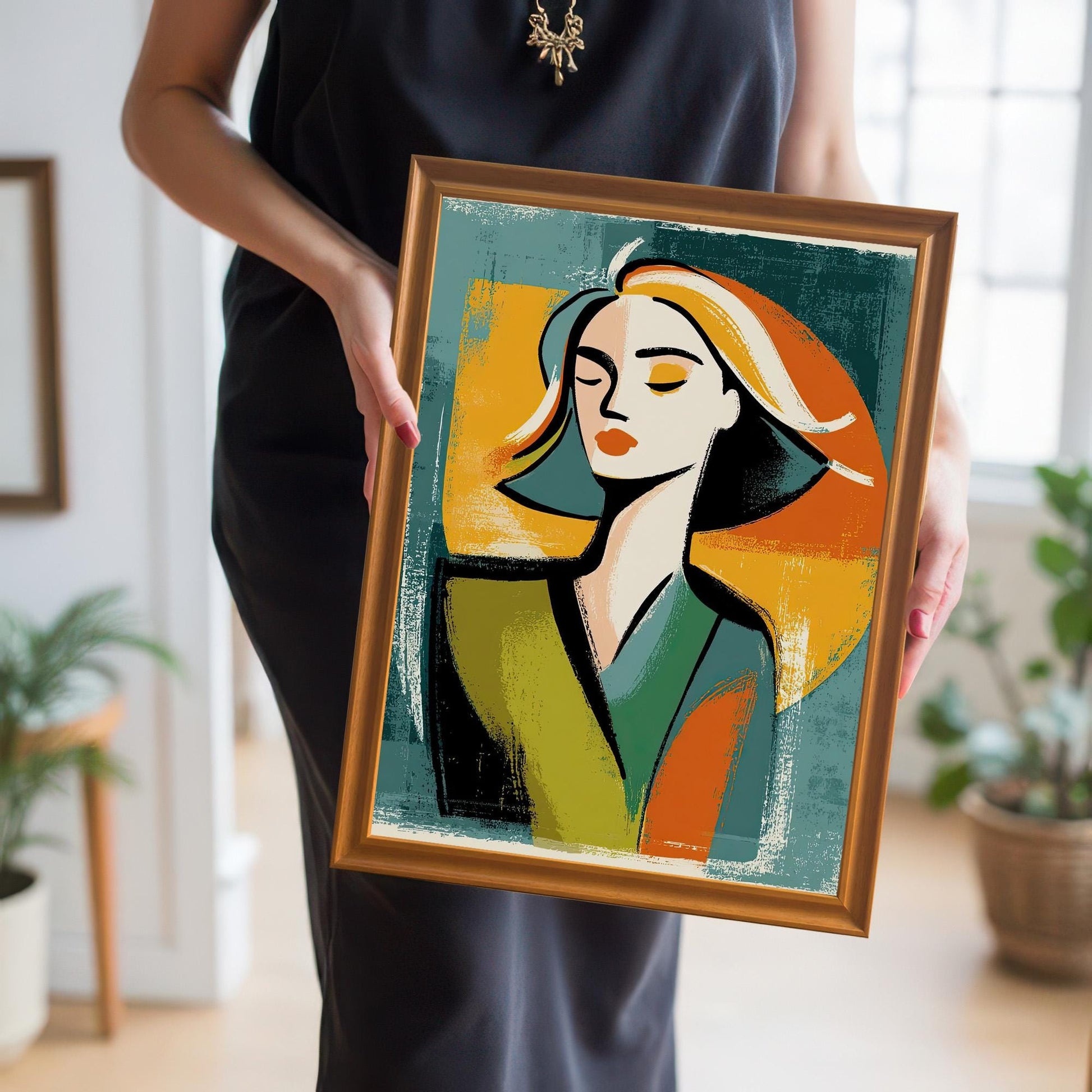 A person in a black dress holding a framed print of a woman's abstract portrait. The frame is a light orange wood color, and the print is held for display.