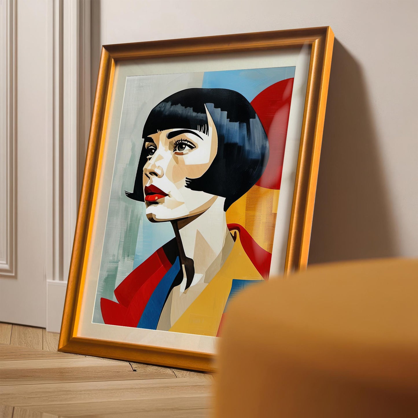 A framed art print of a woman with a bob haircut and red lips leans on the floor against a white paneled wall. The frame is a warm, orange-gold color with a mount.
