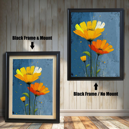 Two framed art prints of yellow and orange flowers on a wooden floor. The print on the left is in a black frame with a mount, and the one on the right is in a black frame without a mount.