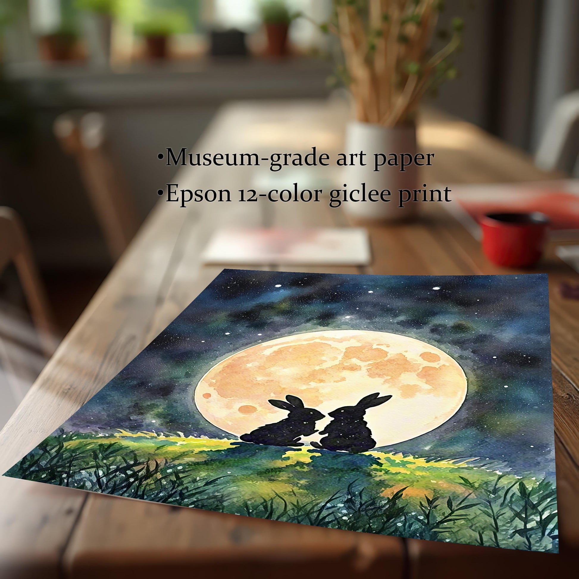 A watercolor print of two rabbits under a full moon, resting on a wooden table, with text describing it as "museum-grade art paper."