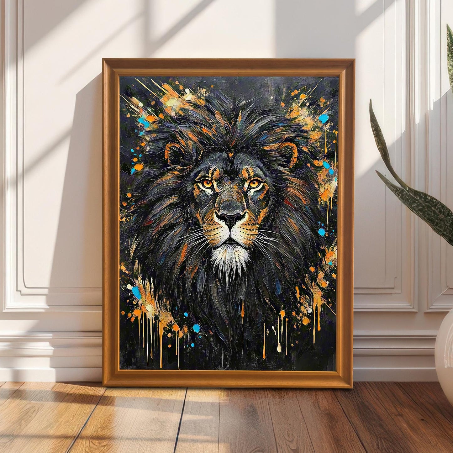 Framed wall art of an abstract lion portrait, leaning against a white paneled wall next to a plant in a white pot.