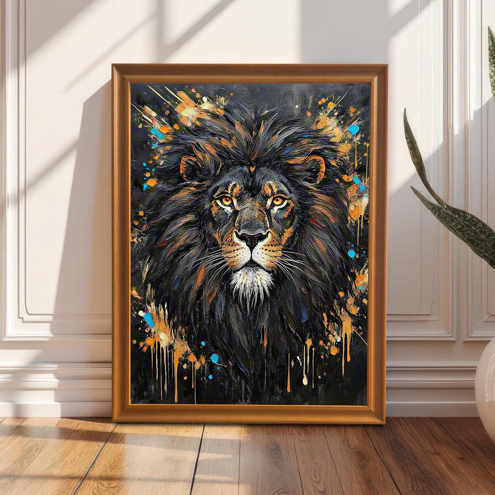 Framed wall art of an abstract lion portrait, leaning against a white paneled wall next to a plant in a white pot.