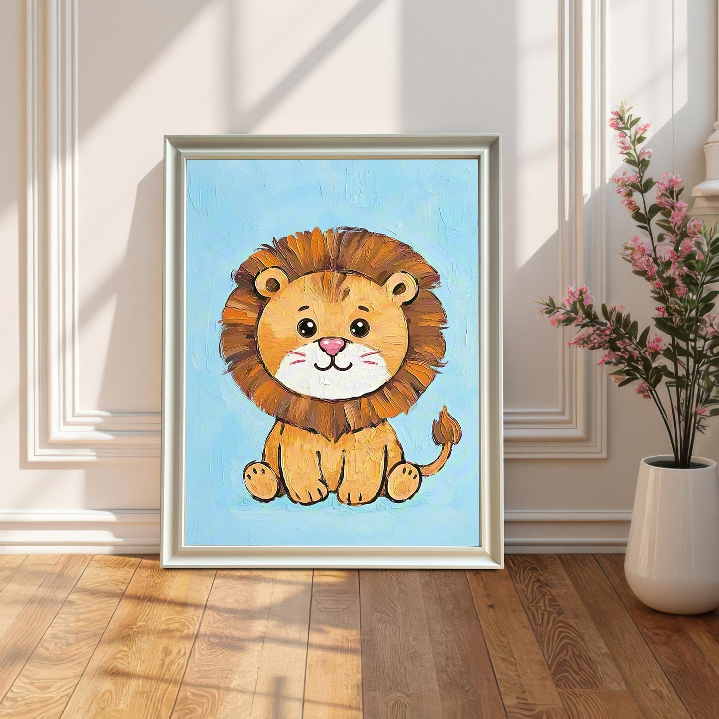 A framed painting of a cute cartoon lion leans on a wooden floor against a white paneled wall, next to a white vase with pink flowers. The frame is white.