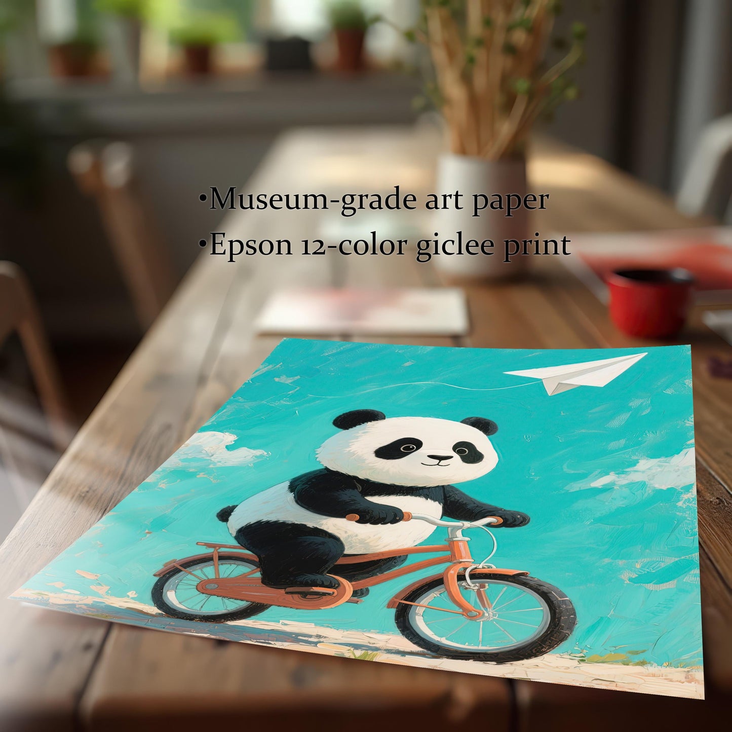 A close-up view of an art print of a panda on a bicycle, lying on a wooden table. The print is slightly curved at the bottom, highlighting the museum-grade paper and giclée print quality.