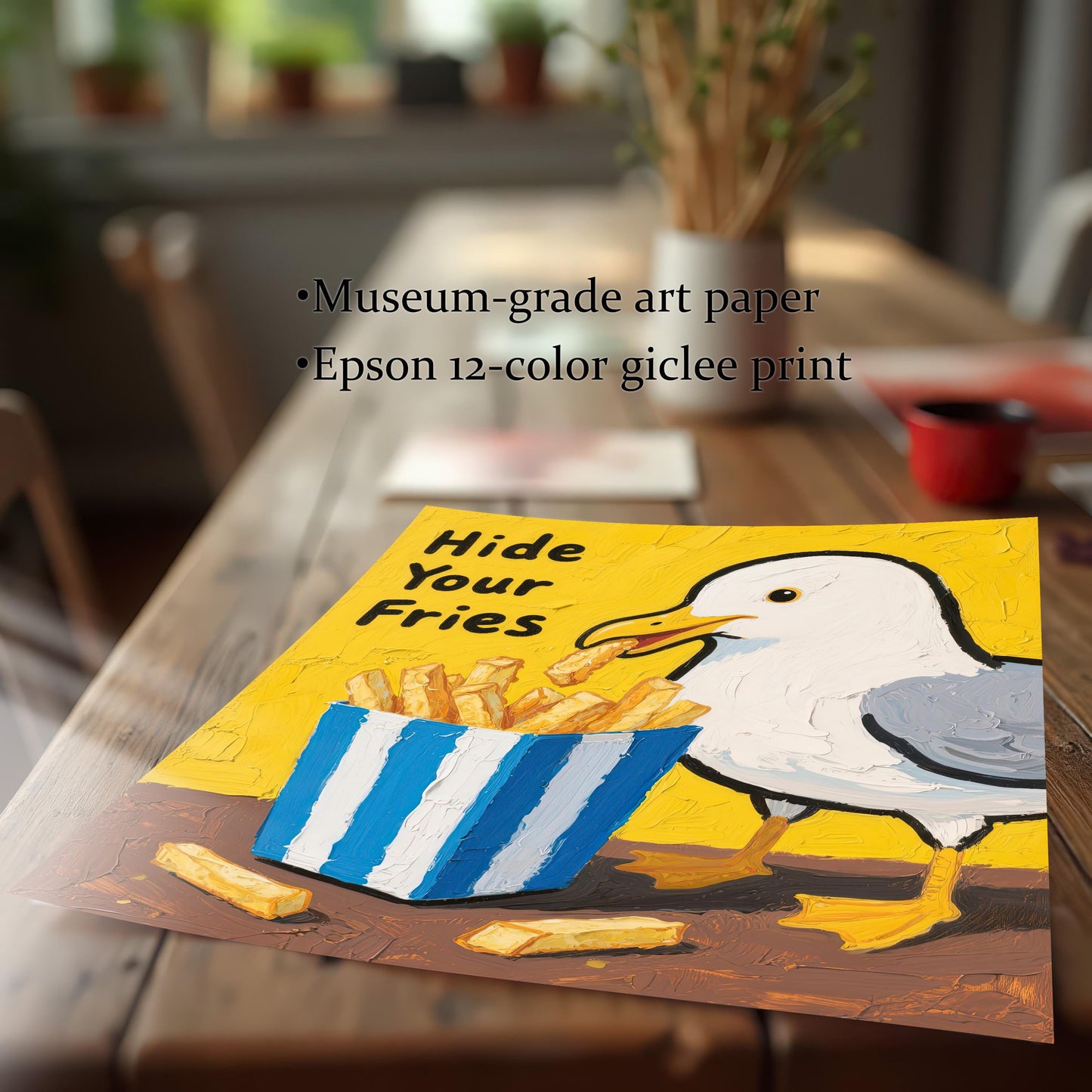 A close-up view of an art print of a seagull and fries, lying on a wooden table. The print is slightly curved at the bottom, highlighting the museum-grade paper and giclée print quality.