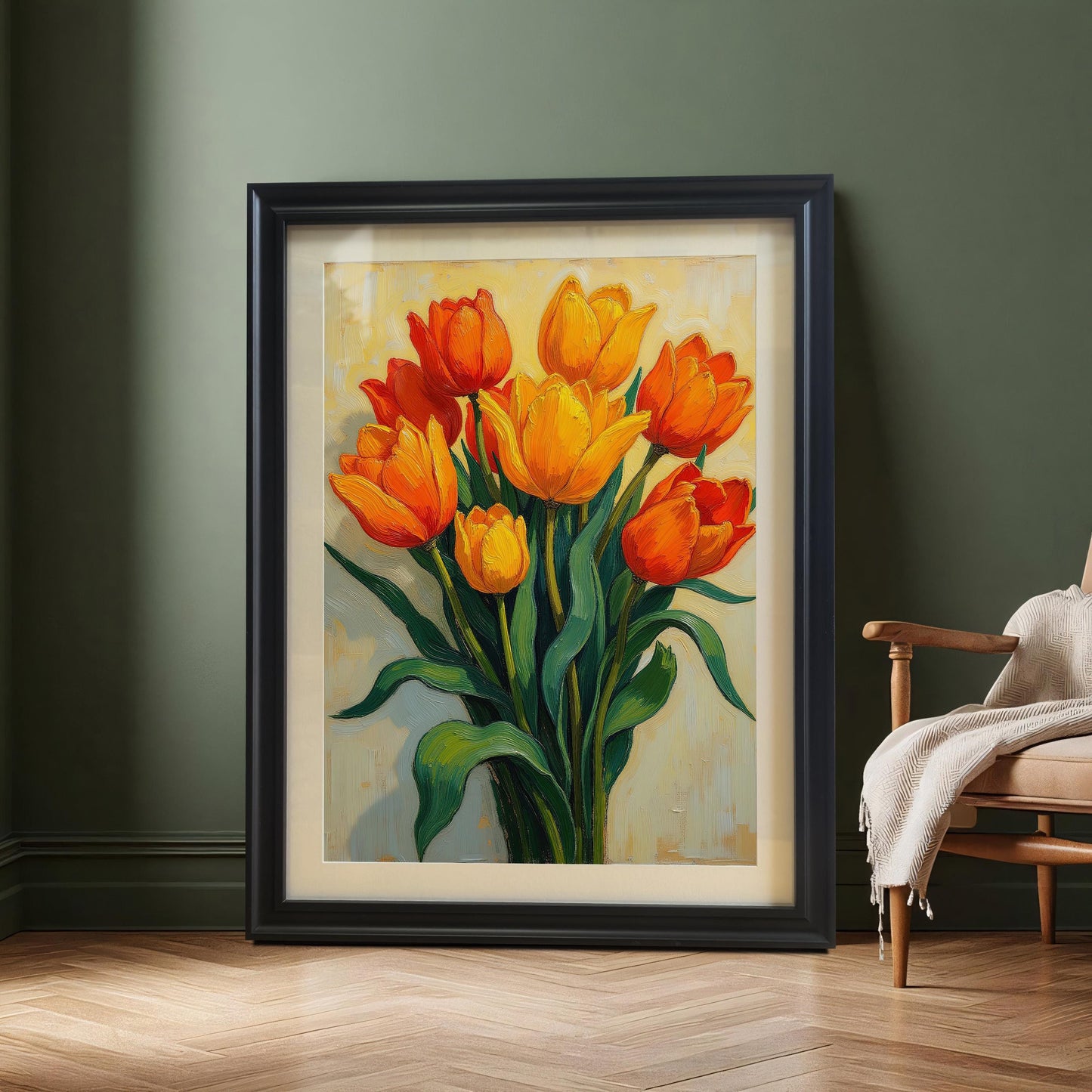 A black-framed painting of a bouquet of orange and yellow tulips leaning against a dark green wall on a light wood floor next to a chair.