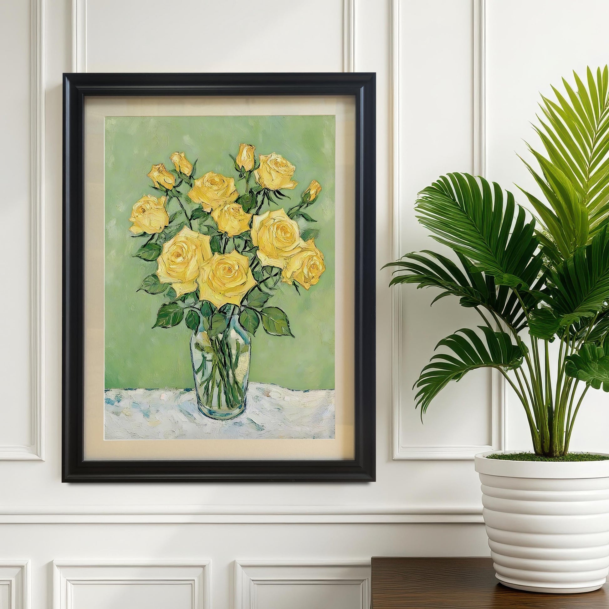 A black-framed art print of yellow roses hangs on a white paneled wall with a potted plant next to it.