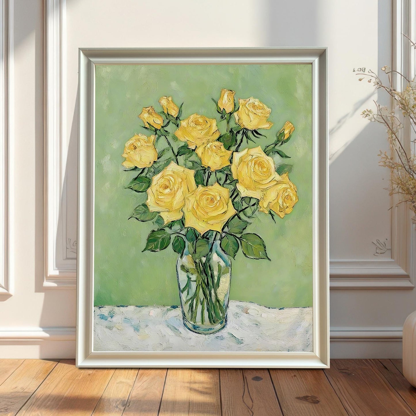 A framed art print of a bouquet of yellow roses in a glass vase leans on a wood floor against a white paneled wall.