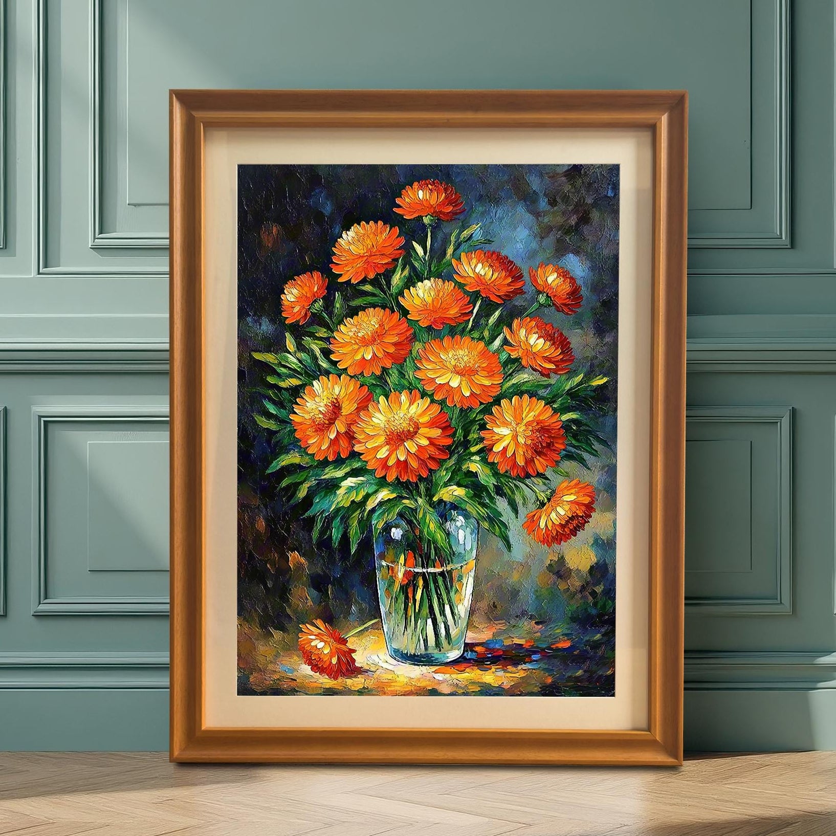A framed art print of a vibrant orange floral bouquet in a glass vase leans on a light wood floor against a dark green paneled wall.