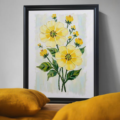 A close-up of a black-framed art print of yellow flowers with a textured, painterly style. Two blurred, yellow pillows are in the foreground.