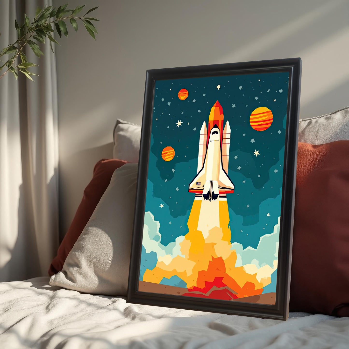 A black-framed print of a rocket ship is leaning against throw pillows on a bed.